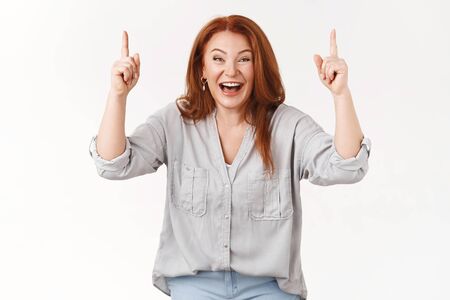 Charismatic good-looking happy lucky redhead middle-aged woman laughing amused joyfully giggle pointing raised hands up awesome hilarious prices good promo look camera excited, white backgroundの写真素材