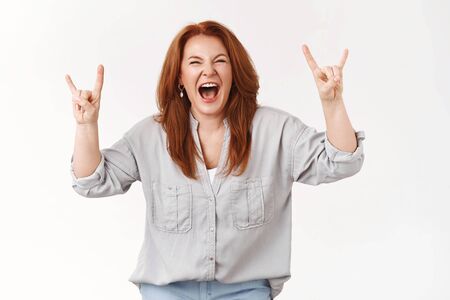 Never too old rock-n-roll. Daring cool redhead middle-aged woman having fun go wild scream out loud positive upbeat mood excited show heavy metal gesture listen loud music, white backgroundの写真素材