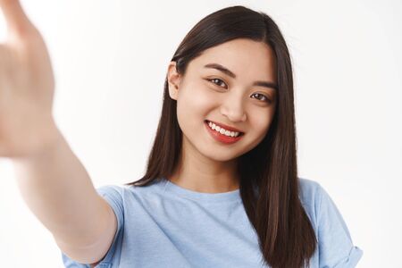 Authentic body-positive shot asian cute tender happy girl extend hand hold camera taking selfie smartphone smiling cheerful express positive upbeat mood have acne prone skin, forehead pimplesの写真素材
