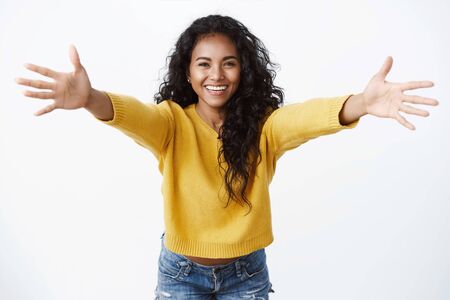 Come here into my arms. Cheerful friendly-looking pretty african american woman in yellow sweater, spread hands in warm welcome, smiling joyfully wanna hug, greeting friend, cuddlingの写真素材