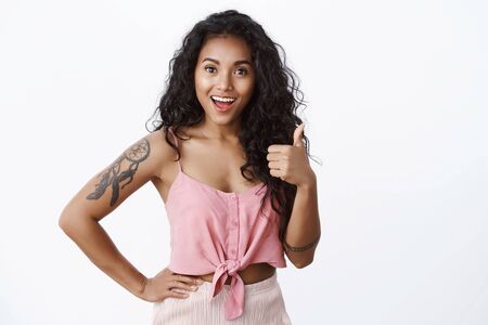 Impressed proud good-looking african-american girl with tattoos, show thumb up and smiling approvingly, nod in agreement, like good idea, encourage friend keep up, standing white backgroundの写真素材