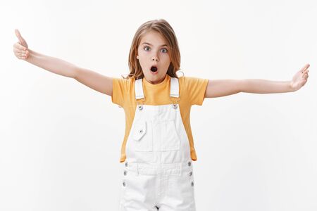 Impressed fascinated cute clever blond girl explain something big, stretch hands showing huge enormous vast product, open mouth and stare camera thrilled, standing speechless white backgroundの写真素材