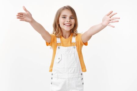 Friendly cheerful young tender blond girl with blue eyes, extend arms and smiling joyfully, wanna cuddle, invite friend give warm hug, welcoming dear guests, stand white backgroundの写真素材