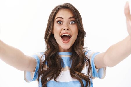 Happy lively cute modern woman looking excited, record video smartphone, hold camera both hands taking thrilled selfie travelling photographing for social media, look surprised amusedの写真素材