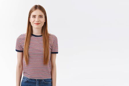 Cheerful good-looking, confident european woman in striped t-shirt with long fair hair, hold hands, act obedient and ready, self-assured can tackle any task, standing white background positiveの写真素材