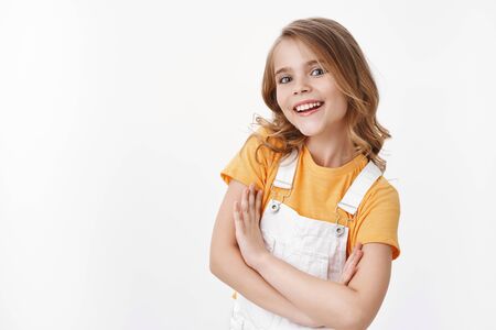 Positive ambitious cute little blond girl, child feeling upbeat and self-assured smiling delighted, look with blue eyes camera, hold hands crossed body confident pose, stand white backgroundの写真素材