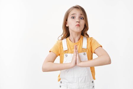 Silly pretty little girl, child begging buy new toy, hold hands pray, supplicating, pouting lips with tender cute gaze, acting lovely and childish, promise do homework after favor, white backgroundの写真素材