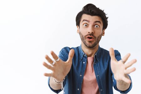 Close-up handsome young bearded man pulling hands forward to take something or hold, asking be careful, worry for friend holding fragile vase, standing white background alarmedの写真素材