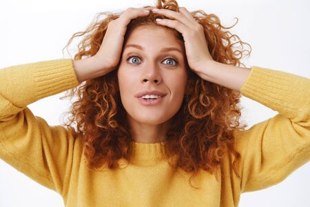 Close-up surprised smiling redhead woman, holding hands on curly hair and gazing camera astonished, grin delighted, cant believe she won, still staring disbelief as receiving comforting good newsの写真素材