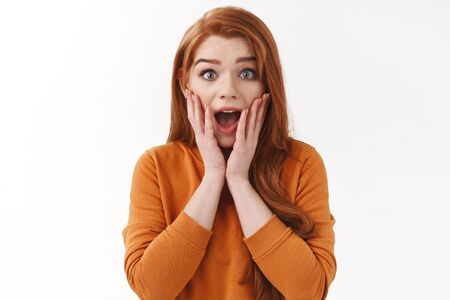 Omg what an awesome promo. Astonished impressed cute redhead silly girl with long ginger hair, open mouth fascinated, gasping wondered say wow touch face from amazement, stare camera speechlessの写真素材
