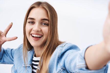 Close-up portrait cute blond teenage girl blogger record video for fans, hold camera with stretched...