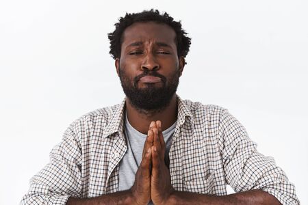 Clingy handsome african american bearded man begging forgiveness or favor, press palms together in pray, pouting, squinting silly, making innocent expression as plead, asking help, white backgroundの写真素材