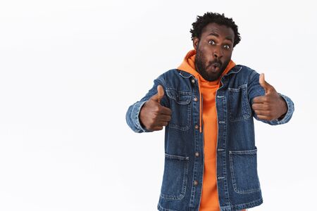 Impressed and fascinated handsome african-american man in denim jacket, hoodie, show thumbs-up in...