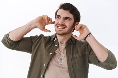 Annoyed young handsome man complaining on noisy neihbours, grimacing face, close ears and looking up...