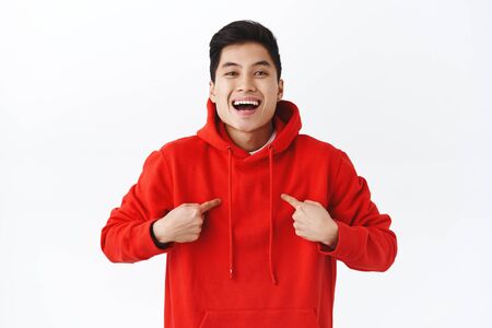 Waist-up portrait of cheerful, confident young asian man asking to participate in event, pointing himself proud and pleased, smiling, becoming champion, talking personal achievementの写真素材