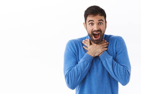 Portrait of speechless, impressed handsome man, lose his speech, gasping and open mouth astonished, smiling amused, hold hands on chest amazed, cant believe something happenedの写真素材