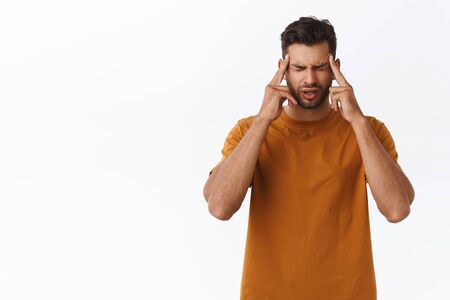 Upset and distressed, tensed young bearded guy suffering terrible migraine, massaging temples with...