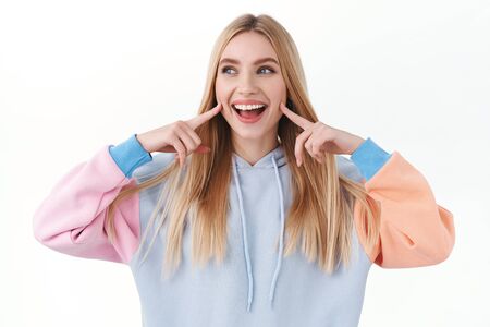 Beauty, lifestyle and fashion concept. Upbeat good-looking blond girl poking her cheeks and smiling,...