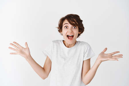 Portrait of surprised caucasian woman spread hands sideways and screaming amazed, looking in awe at...