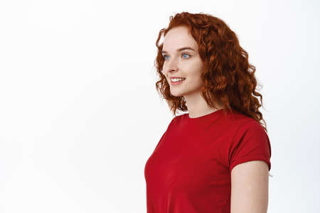 Portrait of young woman with red curly hair and pale smooth skin looking left at empty copy space...