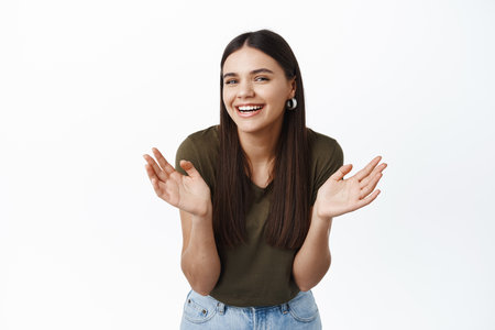 Beautiful candid woman laughing and clapping hands, looking happy at camera with cheerful natural smile, standing against white background in t-shirtの写真素材
