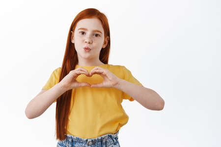 Cute redhead girl with freckles make kissing face and heart sign, I love you gesture, like someone,...