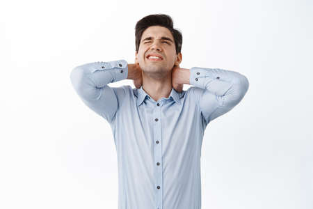Office worker, employee having back pain, touching sore neck and grimacing from painful feeling after sitting at work, have discomfort, standing over white backgroundの写真素材