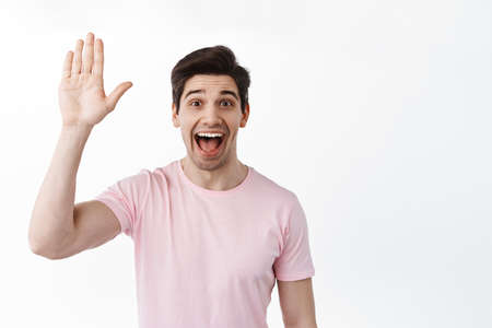 Excited friendly man waving hand and say hey, hello greeting gesture, extremely happy to see you,...