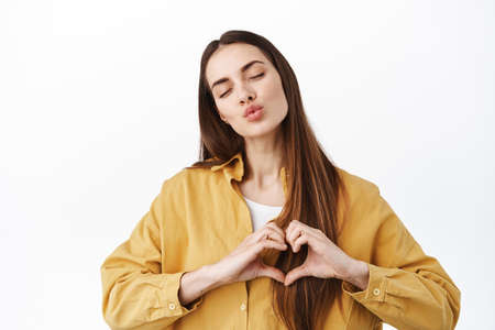 Cute female showing her affection, close eyes and make heart gesture on chest, I love you, sending...