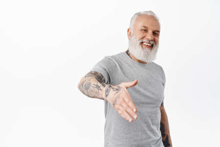 Smiling friendly mature man with tattoos give hand for handshake and laughing, nice to meet you...