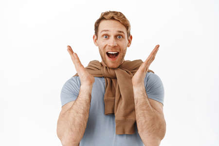 Wow amazing. Happy and excited redhead man gasping fascinated, clap hands and smiling astonished, checking out something awesome and cool, white backgroundの写真素材