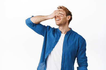 Happy attractive redhead guy cover eyes with hand and smiling, waiting for surprise, anticipating...