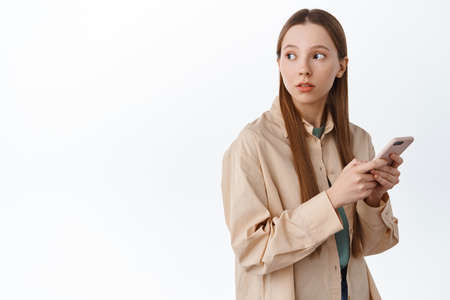 Young female student with long hair, chatting on mobile phone, turn head behind shoulder at copy...