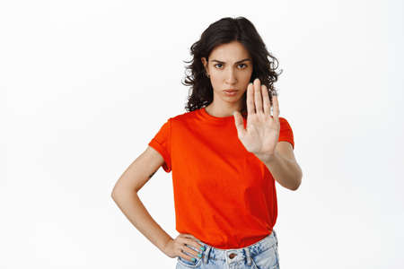 Confident serious woman say no, extend hand to make stop, block sign, prohibit, tell to keep away, remain distance, standing over white backgroundの写真素材