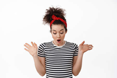 Startled brunette girl drop something, spread hands and looking down in awe, staring bellow at...