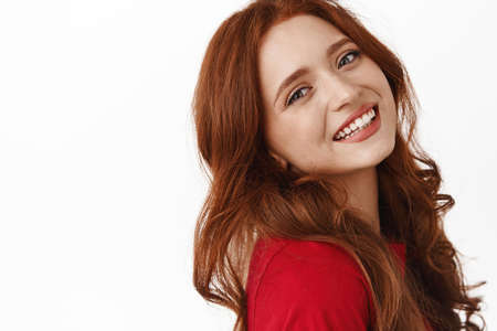 Close up portrait of girl with red curly hair, tilt head and smiling with perfect white smile,...