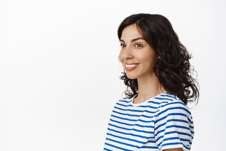 Natural brunette girl with pierced nose and curly hairstyle, looking aside at empty space, white background, wearing striped t-shirtの写真素材