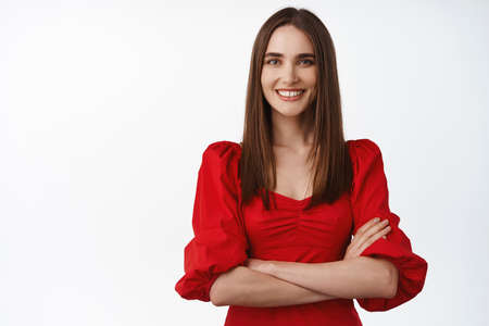 Women beauty. Young happy woman in gorgeous red dress, cross arms on chest confident, smiling white teeth, and looking determined at camera, white backgroundの写真素材