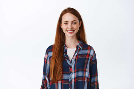 Smiling redhead girl with long hair, pale natural skin no make up, smile white teeth, standing in plaid shirt and looking happy, white backgroundの写真素材