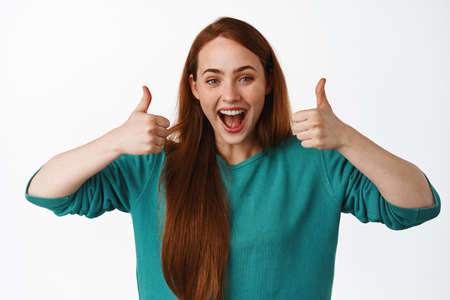 Great job. Happy laughing redhead girl, showing thumbs up in approval, pleased by something cool,...