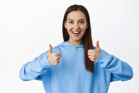 Smiling woman shows support, satisfied, leave positive feedback, nod in approval and show thumbs up,...