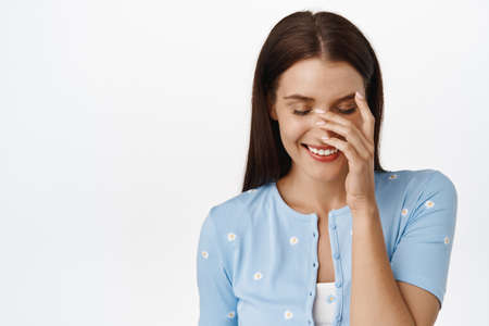 Close up portrait of feminine happy woman, cover face with hand and laughing, looking down with shy...