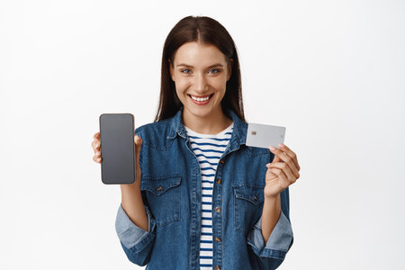 Online shopping. Woman holding blank credit card, showing mobile phone interface, smartphone screen,...