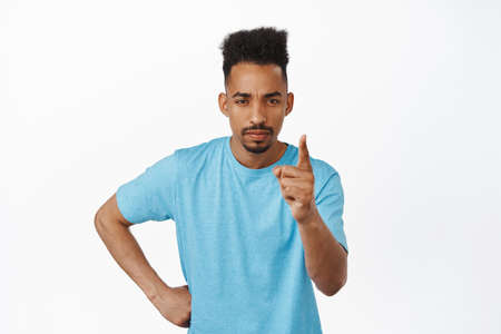 Behave yourself. Serious young african american guy shaking finger to scold you, frowning and...