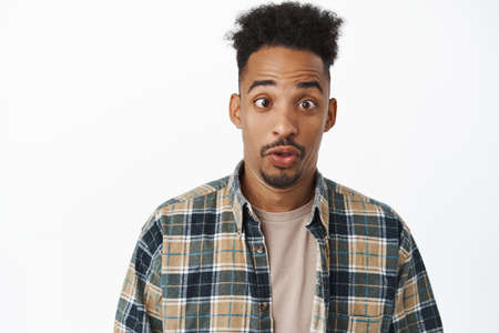 Close up shot of funny and silly african american guy with curly afro hair, squinting, pucker lips,...