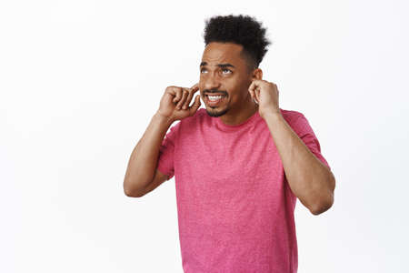 African american guy bothered by loud neighbours. Young man shut ears with fingers, clench teeth and...