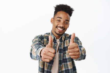 Happy and positive african american man showing thumbs up, smiling satisfied, praise excellent great...