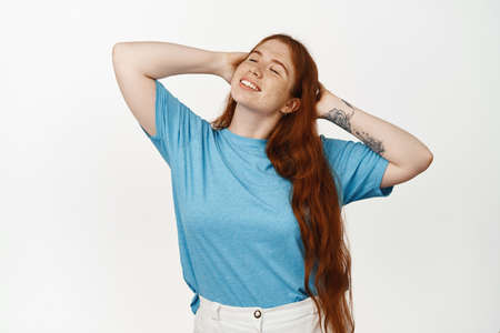 Portrait of resting happy girl with long red hair sunbathing, relaxing under sun, close eyes and holding hands behind head, lying with eyes closed and carefree smile, white backgroundの写真素材