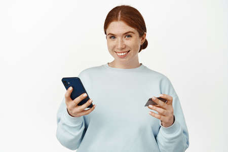 Online shopping. Beautiful young woman shops on website, app, paying with mobile phone and credit...