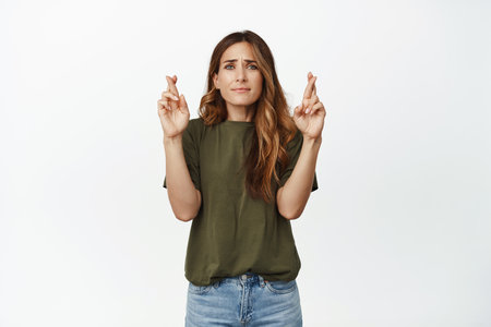 Hopeful caucasian woman, middle aged female model cross fingers, praying, hoping for wish come true, looking concerned, waiting for results, white backgroundの写真素材